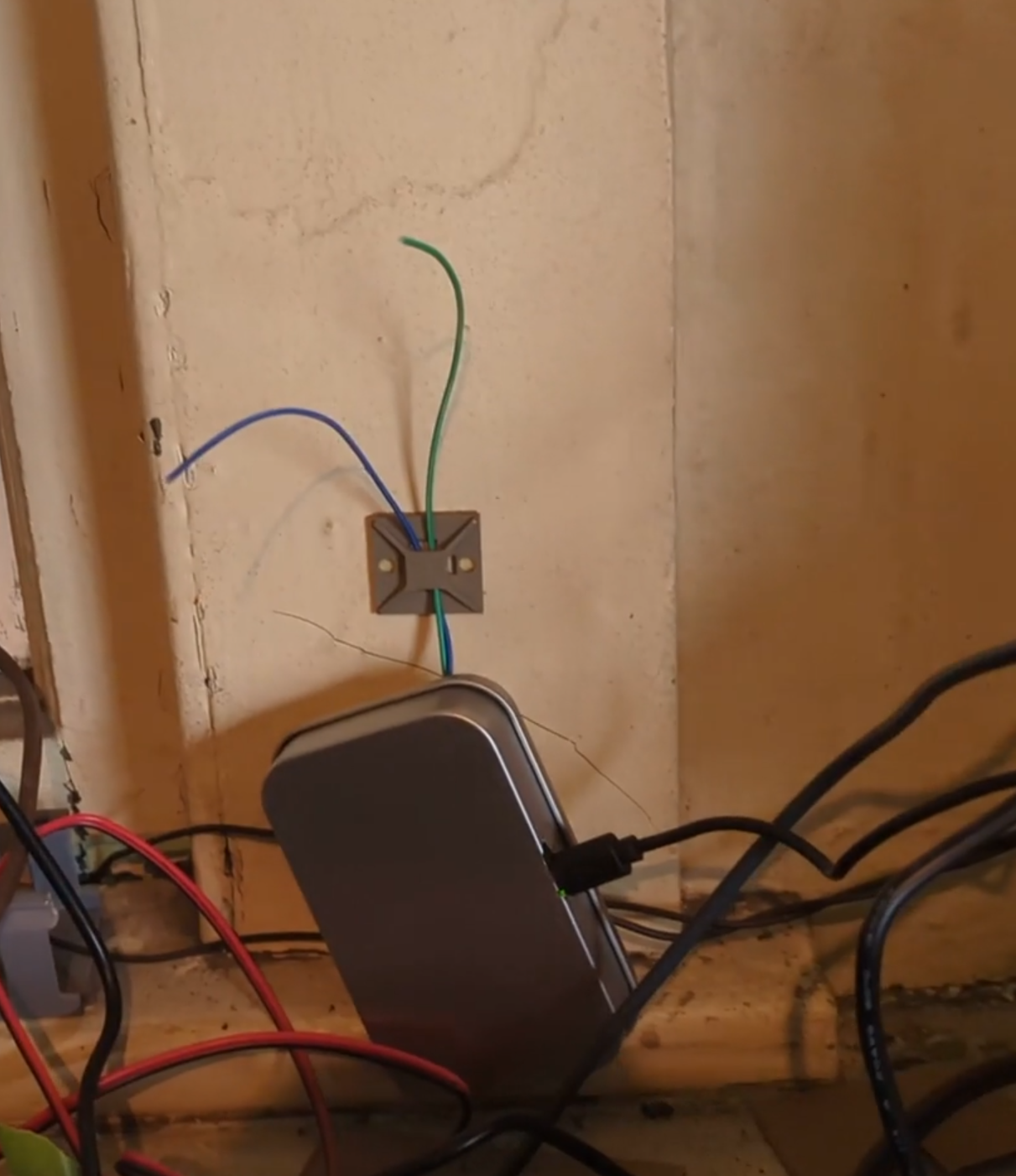 A metal box with exposed wires in front of a window. Other wires are visible below it.