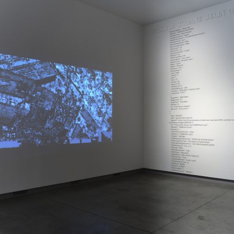 A grainy black and white image projected on a wall, another wall to the right is covered in metadata.